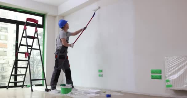 Malíř maluje stěnu bílou s válečkem. Malba stěny nebo strop v bytě - Záběry, video