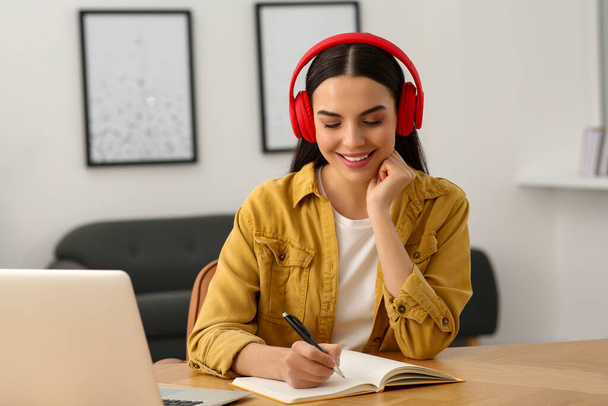 Online translation course. Student in headphones writing near laptop at home - Fotoğraf, Görsel