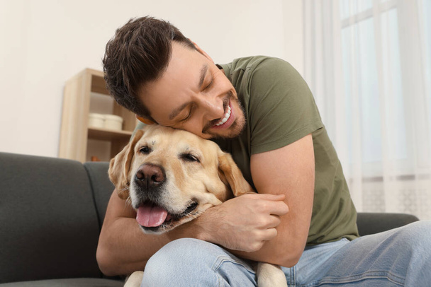 Man hugging his cute Labrador Retriever on sofa at home - Foto, Imagem