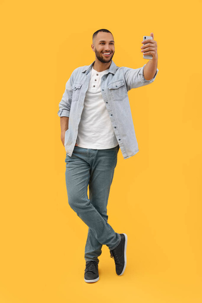 Smiling young man taking selfie with smartphone on yellow background - Foto, imagen