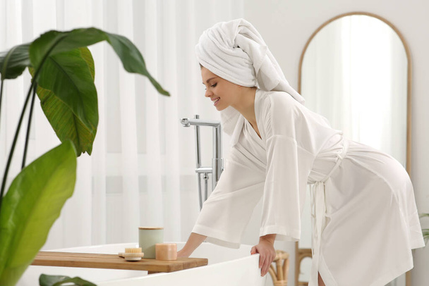 Beautiful happy woman wearing white robe near tub in light bathroom - Foto, afbeelding