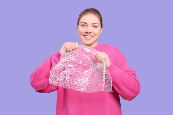 Woman popping bubble wrap on purple background. Stress relief - Foto, afbeelding