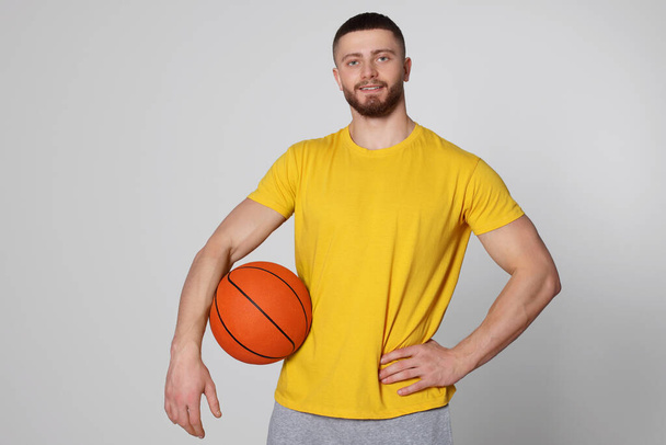 Athletic young man with basketball ball on light grey background - Фото, изображение