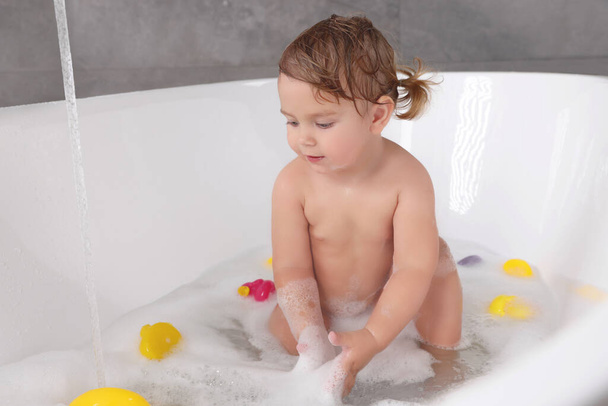 Cute little girl taking bubble bath with toys indoors - Photo, image