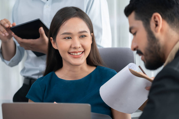 Young Asian businesswoman poses confidently with diverse coworkers in busy meeting room background. Multicultural team works together for business success. Office lady portrait. Concord - Foto, Imagen