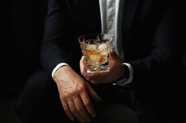 Man holding glass of whiskey with ice cubes on black background, closeup - Fotoğraf, Görsel