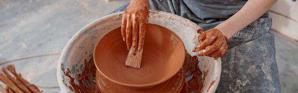 Blick von oben auf die Hände einer Kunsthandwerkerin, die ein Töpferinstrument in der Hand hält und im Bastelatelier Tonschalen formt - Foto, Bild