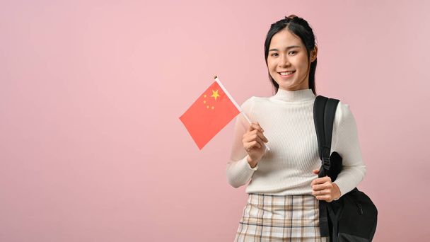 Aziatisch meisje tonen een China vlag op roze geïsoleerde achtergrond, onderwijs concept. studeren in het buitenland. - Foto, afbeelding