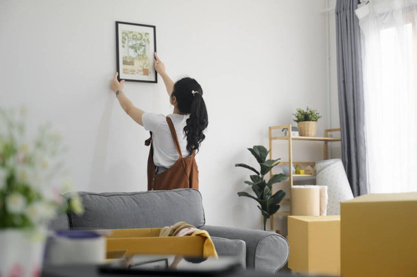 jong aziatisch vrouw versieren nieuw huis terwijl verhuizen naar nieuw huis of appartement. - Foto, afbeelding