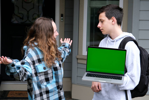 teenagers in hands with laptop and a backpack green screen chromakey girl surprised spread her arms to the sides boy looks at look at each other friends classmates advertising shock space for text - Photo, Image