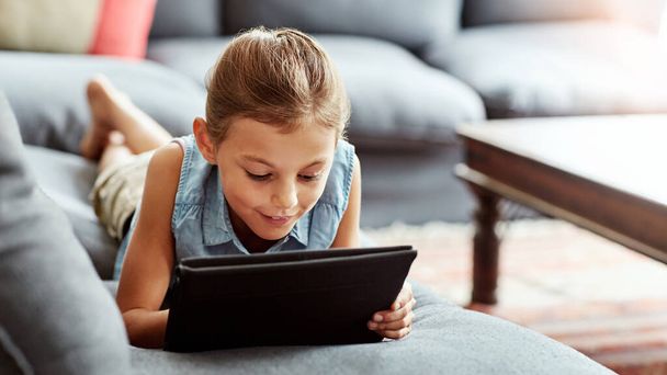 Είναι περίεργη για τη σύγχρονη τεχνολογία. ένα μικρό κορίτσι που χρησιμοποιεί ένα ψηφιακό tablet στο σπίτι - Φωτογραφία, εικόνα