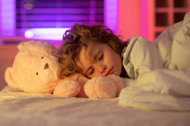 Night sleep. Kid sleeps with a toy teddy bear on bed, napping. Cute child sleeping - Zdjęcie, obraz