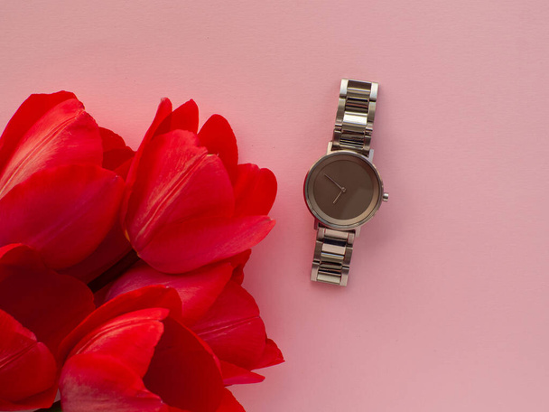 Womens hand watch on pink background with tulip flowers and copy space. Womens, Valentines and Mothers Day gift. Concept of beauty, elegance and femininity. Buying birthday gifts. Shopping and sale. - Foto, Bild