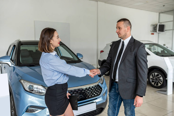 smiling car salesman shakes the hand of a brunette who wants to buy a car. The interior of the car. There are many different modern cars around. - Φωτογραφία, εικόνα