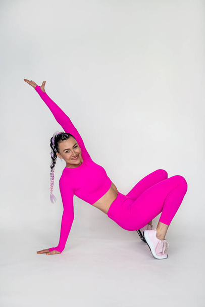 Slim brunette doing yoga and stretching exercises in crimson leggings isolated on white wall. sport. stretching - Foto, Imagem