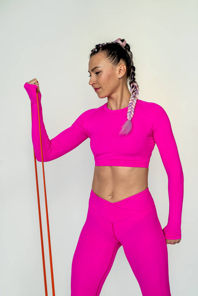 красивый снимок молодой женщины в розовой спортивной одежде делать упражнения с сопротивлением полосы изолированы на белом фоне. спорт как здоровый образ жизни. спортивное тело - Фото, изображение