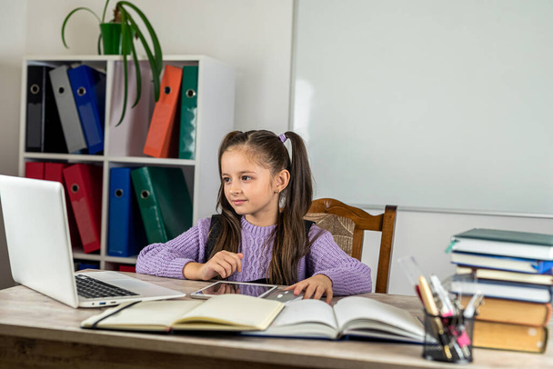 Retrato de uma menina bonita na sala de aula em uma mesa com livros e um computador. o conceito de aprendizagem. Escola. horário escolar - Foto, Imagem