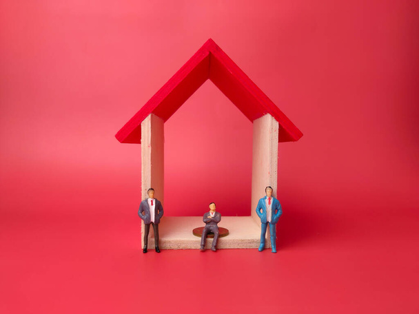 Spielzeughaus mit Miniaturmenschen auf rotem Hintergrund. Geschäftskonzept. - Foto, Bild