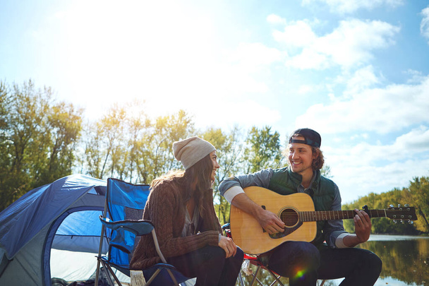 Musik ist ein Ausbruch der Seele. ein junger Mann spielt seiner Freundin beim Zelten ein Lied auf seiner Gitarre - Foto, Bild