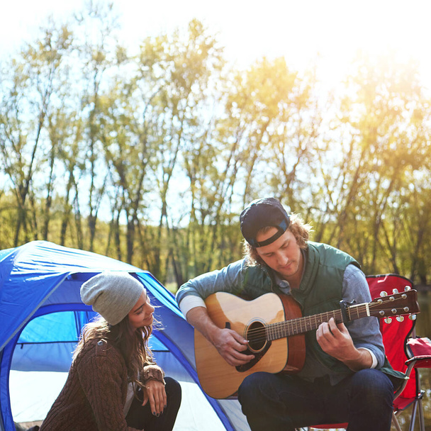 Ich kann es einfach nicht mehr für mich behalten. ein junger Mann spielt seiner Freundin beim Zelten ein Lied auf seiner Gitarre - Foto, Bild
