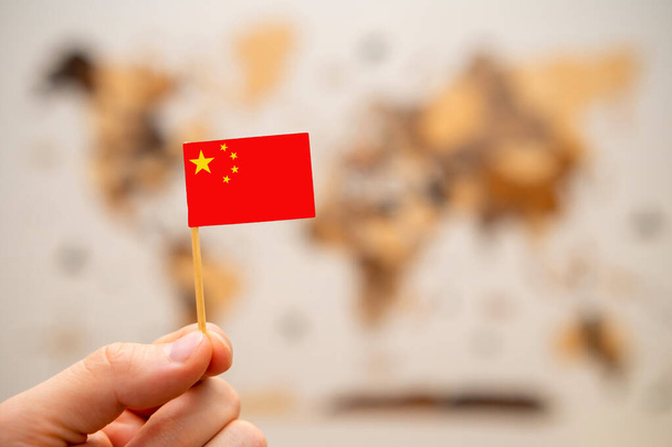 China flag in mans hand on the wooden world map background. Global economy and geopolitics concept.  - Photo, Image