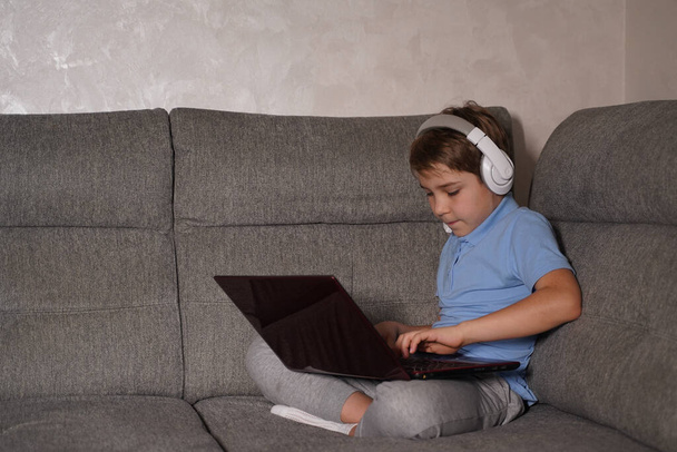Chłopak w bezprzewodowych słuchawkach e-learning na laptopie w domu. Nauka na odległość online - Zdjęcie, obraz