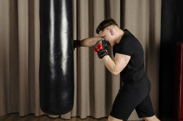 Boxer training with a punching bag in a cozy beige studio, throwing a punch. - Foto, imagen