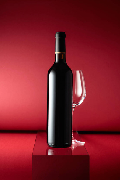 Bottle of red wine and an empty wine glass on a red background. - Fotó, kép