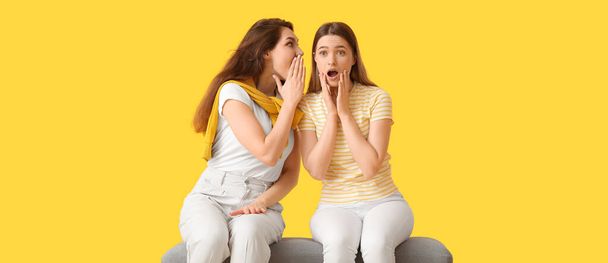 Νεαρές κουτσομπολεύουν γυναίκες σε κίτρινο φόντο - Φωτογραφία, εικόνα