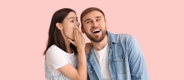 Young woman telling secret to her boyfriend on pink background - Photo, Image
