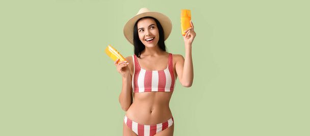 Pretty young woman with sunscreen creams on green background - Foto, imagen