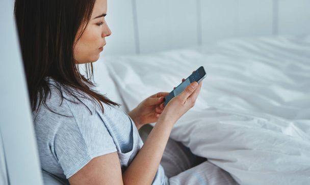 Checking her messages. High angle shot of an attractive young woman reading her text messages while lying in bed - Foto, imagen