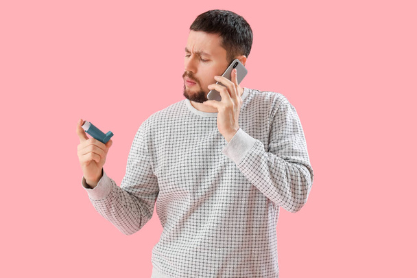 Sick man with inhaler talking by phone on pink background - Valokuva, kuva