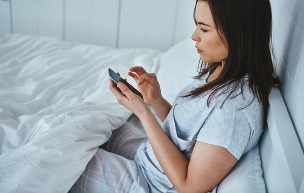 SMS-re ébredek. Nagy látószögű felvétel egy vonzó fiatal nő olvassa szöveges üzeneteket, miközben fekszik az ágyban - Fotó, kép