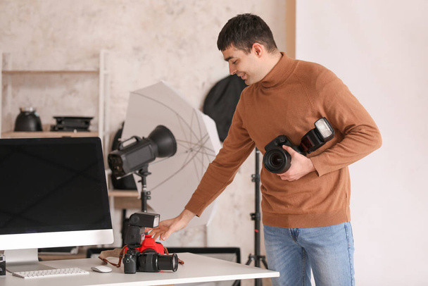 Νεαρός άνδρας φωτογράφος με επαγγελματικές φωτογραφικές μηχανές στο στούντιο - Φωτογραφία, εικόνα