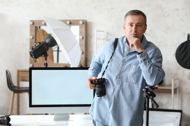 Зрелый фотограф с профессиональной камерой и компьютером в студии - Фото, изображение