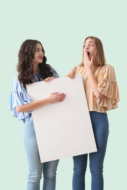 Young women with big blank poster on mint background - Photo, Image