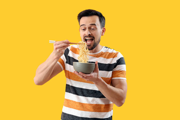 Handsome man with bowl of Chinese noodles on yellow background - Zdjęcie, obraz