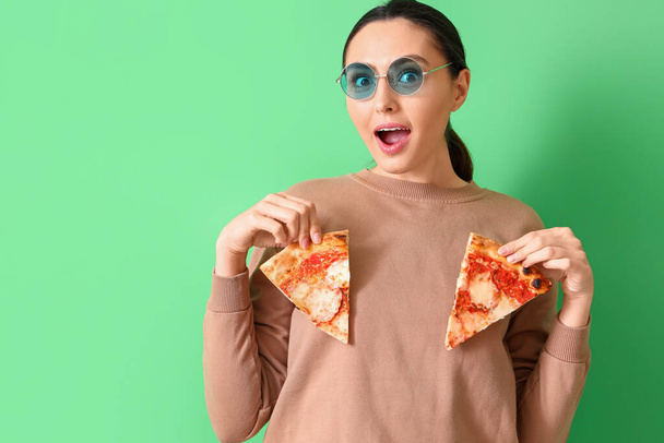 驚くべき若いです女性でサングラスでスライスのおいしいピザで緑の背景 - 写真・画像