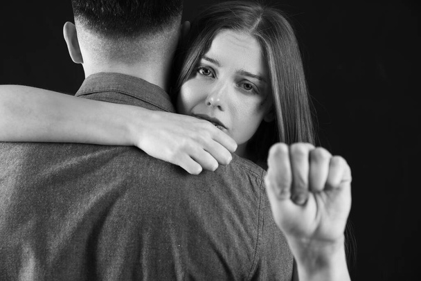 Bruised young woman with her husband showing fist on dark background. Domestic violence concept - Fotoğraf, Görsel