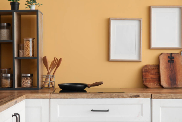 Mostradores con sartén, estufa y utensilios de cocina cerca de la pared amarilla - Foto, Imagen