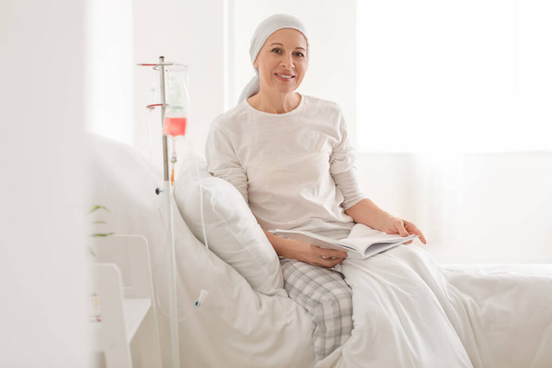 Зрелая женщина после химиотерапии читает книгу в клинике - Фото, изображение