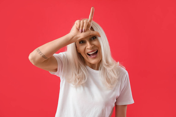 Mature woman showing loser gesture on red background - Photo, image