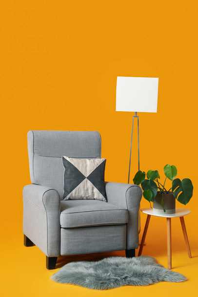 Acogedor sillón gris, lámpara y mesa con planta de interior sobre fondo naranja - Foto, Imagen