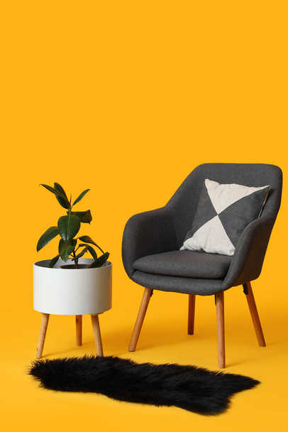 Stylish grey armchair, houseplant in pot and fur rug on orange background - Fotó, kép
