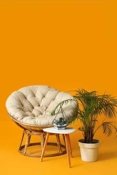Cozy armchair, table and houseplants on orange background - 写真・画像