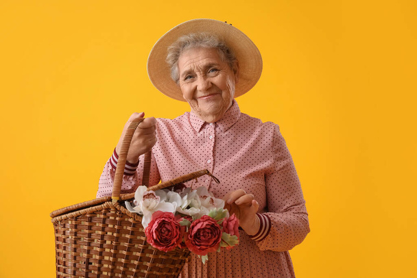 Femme âgée avec panier de fleurs sur fond jaune - Photo, image