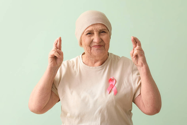 Seniorin nach Chemotherapie mit rosafarbener Schleife, die Daumen auf grünem Hintergrund drückt. Brustkrebs-Konzept - Foto, Bild