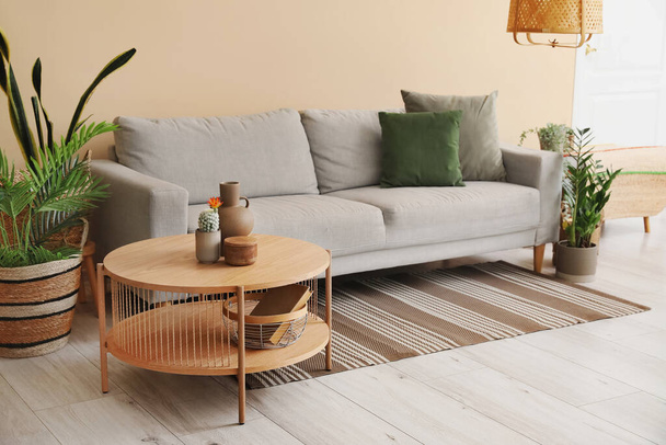 Интерьер светлой гостиной с уютным серым диваном, журнальным столиком и комнатными растениями - Фото, изображение
