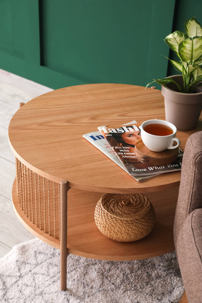 Coffee table with cup of tea, magazines and houseplant near armchair in living room - Foto, Imagem